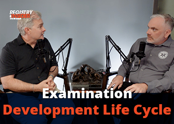 Two men are seated and discussing topics related to the "Examination Development Life Cycle," with microphones in front of them.