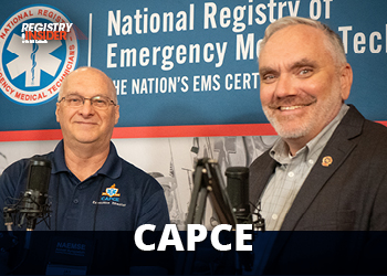 Two men stand in front of a backdrop featuring the National Registry of Emergency Medical Technicians. They are smiling and posing for the photo.