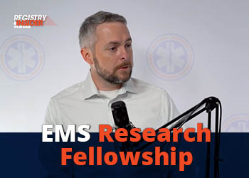 A man speaks into a microphone, promoting an EMS Research Fellowship, with a logo in the background.