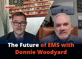 Two men are engaged in a video discussion about the future of EMS, with a backdrop of various emblems and a professional setting.